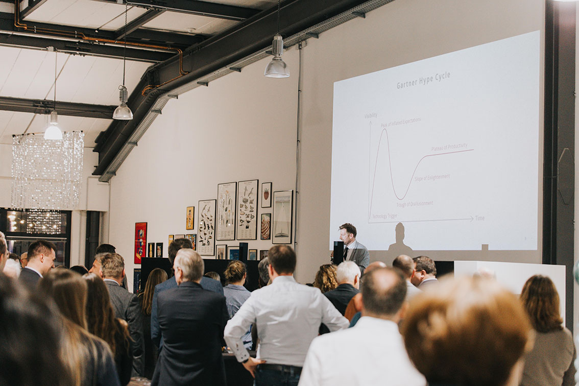 Peter Bossecker gives a presentation about AI at the 55 Year anniversary event. A slide titled 'Gartner Hype Cycle' can be seen in the background.