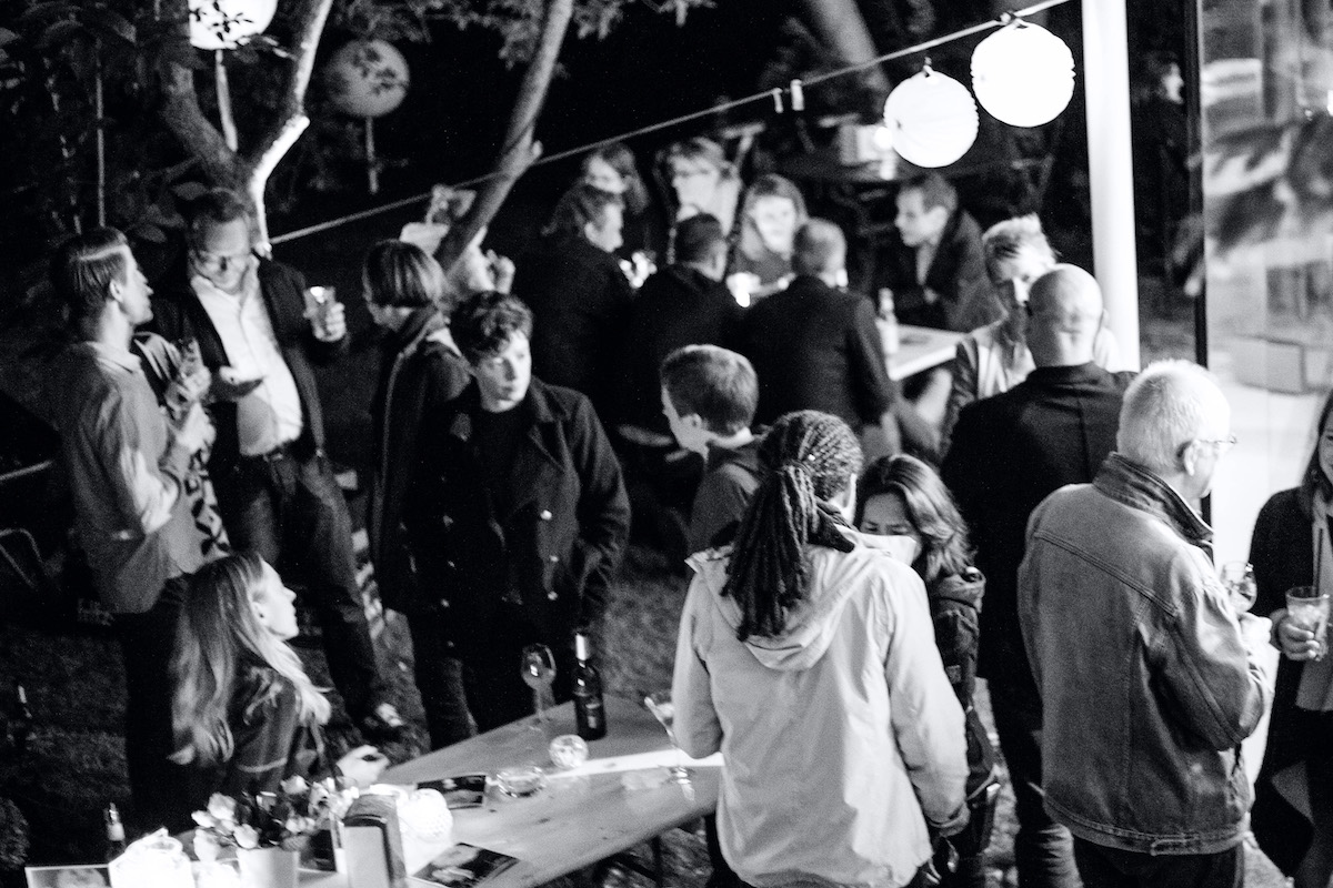 The team during a summer party, chatting an drinking in the garden, with paper lanterns overhead.